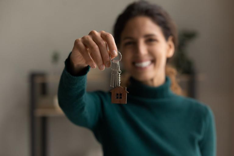 A landlord holding out keys with a wooden house keyring and smiling