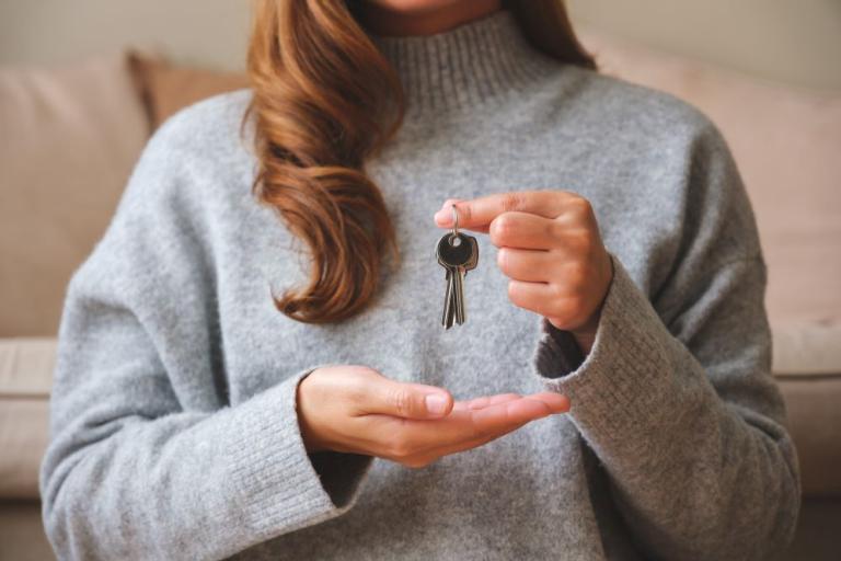 A property manager in a grey jumper holds keys in one hand, with her other hand hovering underneath