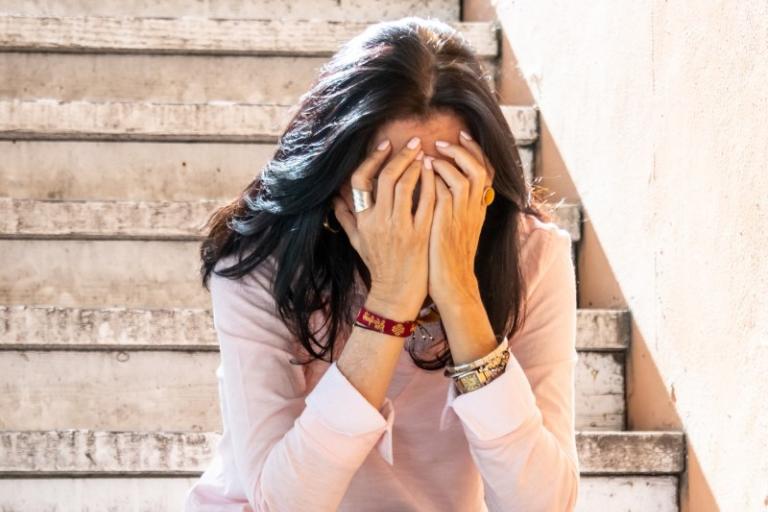 A woman illegally evicted covers her head in her hands, sitting on stairs outside